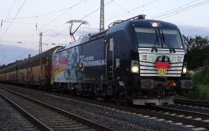 Eine für den Tag der Deutschen Einheit lackierte Siemens VECTRON der Eisenbahnlogistikers MRCE vor einem Autozug der PCT Private Car Train GmbH (PCT)