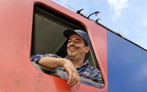 Lokführer mit Basecap und Schnautzer schaut verschmitzt aus Fenster einer Lok.