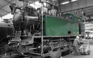 Frau führt letzte Handgriffe an einer fast fertig aufgearbeiteten Schmalspur-Lokomotive aus