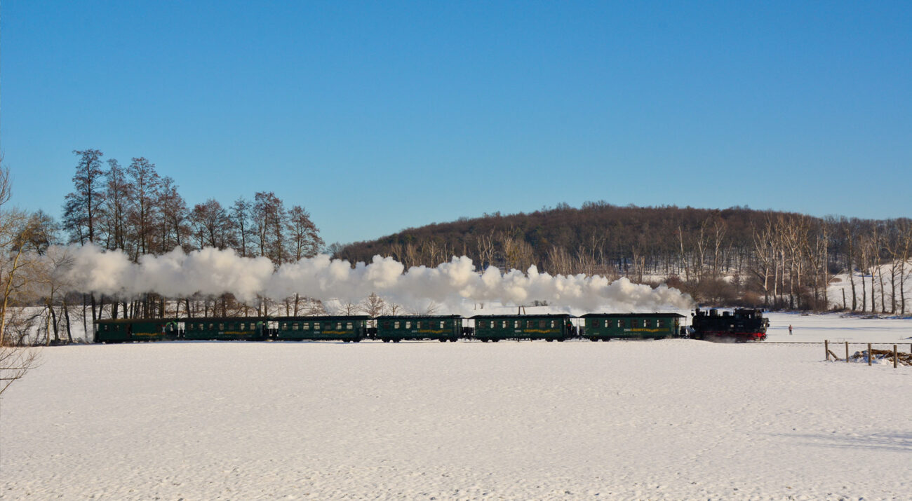 Lößnitztalbahn dampft durch weiße Schneelandschaft bei blauem Himmel